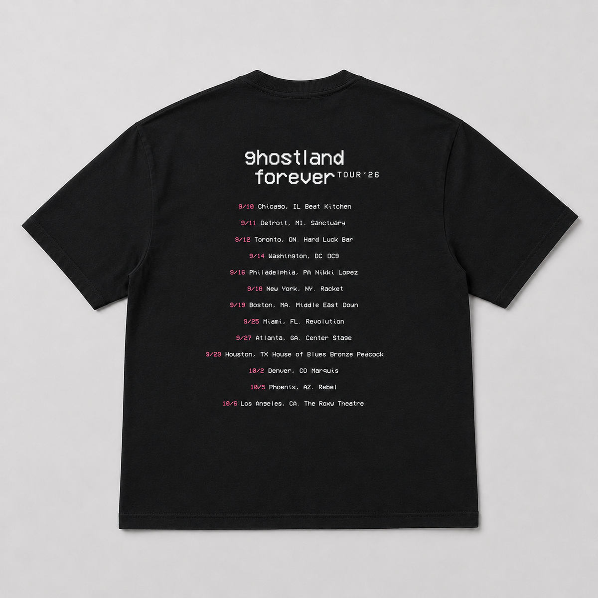 A black short-sleeve t-shirt laid flat against a light gray background, featuring a white and pink printed concert tour schedule for Ghostland Forever Tour '26 on the front.