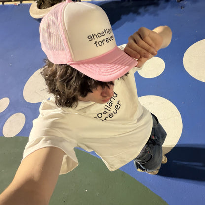 A person wearing a pink and white trucker hat with the text 'ghostland forever' and a matching white t-shirt, photographed from a high-angle perspective on a blue and white polka-dot surface.